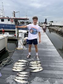 A young angler proudly displaying a large fish alongside a catch of multiple smaller fish on the dock after a successful fishing trip.