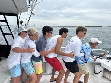 A group of young anglers excitedly reeling in a catch aboard a fishing charter, showcasing teamwork and enthusiasm on the water.
