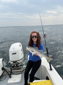 An angler proudly displaying a striped bass while fishing on a boat, showcasing a successful day on the water.