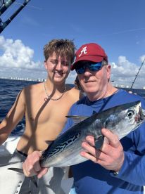 A young angler and an adult proudly displaying a large Bonito while fishing offshore, enjoying a sunny day on the water.
