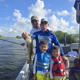 A family enjoying a successful day of fishing, showcasing a large Largemouth Bass caught on a scenic waterway.