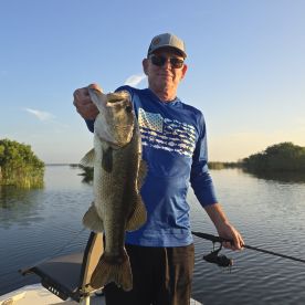 An angler proudly displaying a large Largemouth Bass while fishing on a serene lake during sunset.