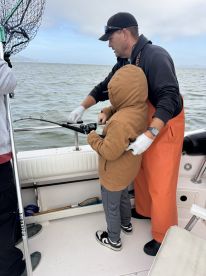 A young angler is learning to reel in a fish with the guidance of an experienced adult on a fishing boat, showcasing a hands-on fishing experience.