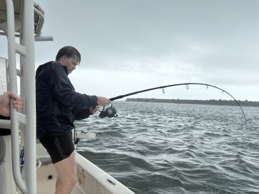 A young angler reeling in a catch during a fishing trip on a cloudy day, showcasing the excitement of fishing in a dynamic environment.