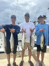 Three anglers proudly displaying their catch of King Mackerel after a successful fishing trip, with a boat visible in the background.