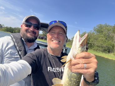 Two anglers posing with a Northern Pike while enjoying a sunny day on the water.