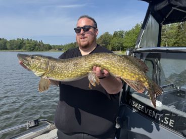 Angler proudly displaying a large Northern Pike while fishing on a serene lake.