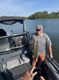 An angler proudly displaying a Northern Pike while fishing from a boat in a serene lake setting.