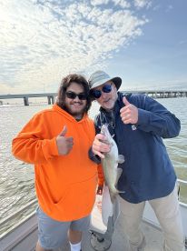 A young angler and an experienced fisherman celebrate a successful catch of a Speckled Trout while fishing from a boat.