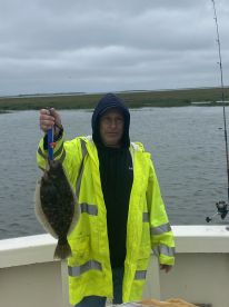 Angler proudly displaying a Flounder while fishing on a boat in a coastal environment.