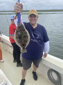 An angler proudly displaying a large Flounder while fishing on a charter boat in a coastal environment.