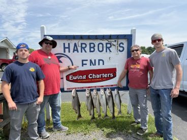 Group of anglers proudly displaying their catch of Lake Trout in front of Ewing Charters sign at Henderson Harbor.