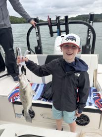 Young angler excitedly holding a striped bass while fishing from a boat, showcasing a fun day on the water.
