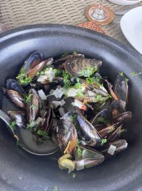 A dish featuring mussels garnished with herbs and onions, presented in a bowl, likely part of a seafood meal.