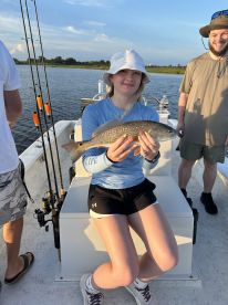 A young angler proudly displaying a Redfish while seated on a boat, enjoying a scenic fishing trip.