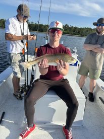 A young angler proudly displaying a Redfish while fishing on a boat, with fellow anglers enjoying the day on the water.