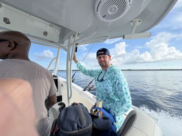 Two anglers aboard a center console boat, preparing for a fishing trip in calm waters, showcasing the boat's interior and helm area.