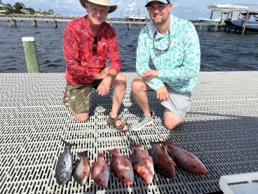 Two anglers proudly displaying their catch of Red Snapper and a Blackfin Tuna on a dock after a successful fishing trip.