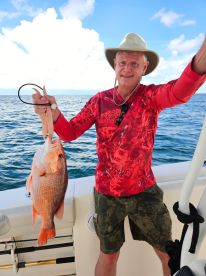 An angler proudly displaying a large Red Snapper while fishing offshore, showcasing a vibrant ocean backdrop.