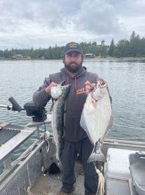 Angler proudly displaying a large Salmon and Halibut while fishing in a scenic coastal environment.