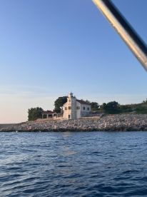 Scenic view of a lighthouse on the shoreline, captured from a boat during a fishing trip, showcasing the tranquil waters and clear sky.