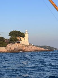 A scenic view of a lighthouse on a rocky shore, captured from a boat in calm waters, showcasing the beautiful coastal landscape.