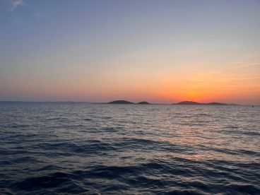 A serene sunset view over calm waters, with distant islands silhouetted against the colorful sky.