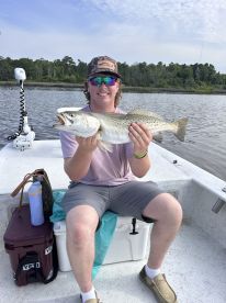 A young angler proudly displaying a large Speckled Trout while fishing from a boat in a calm waterway.