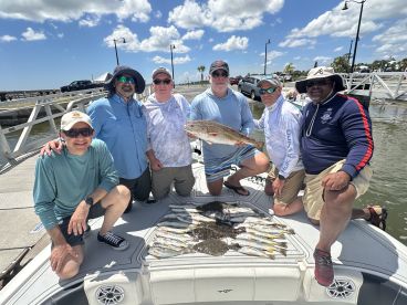 A group of anglers proudly displaying their catch, including several Speckled Trout and a Redfish, on a boat after a successful fishing trip.