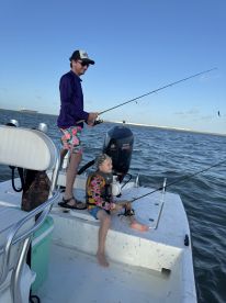 A father and son enjoy a fishing trip on a boat, with the child actively engaged in fishing while wearing a life jacket.