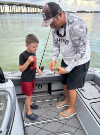 A young boy watches intently as an adult shows him a caught fish on a boat, highlighting a memorable fishing experience.