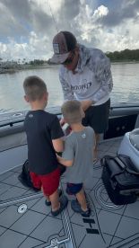 Two young anglers observing a fishing guide as he demonstrates handling a fish on a modern fishing boat.