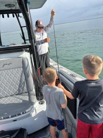 Two young boys excitedly watching as an angler reels in a fish on a Yellowfin boat, showcasing a fun family fishing experience.