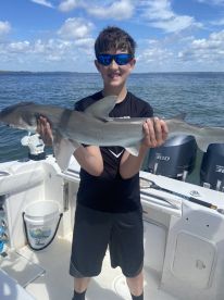 A young angler proudly displaying a caught shark while aboard a boat, enjoying a sunny day on the water.