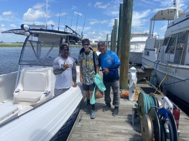 Three anglers posing on the dock next to a fishing boat, showcasing a sunny day on the water.