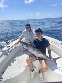 Two anglers aboard a boat proudly displaying a large King Mackerel caught during a deep-sea fishing trip.