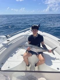 A young angler proudly displaying a large King Mackerel while seated on a boat in open waters.