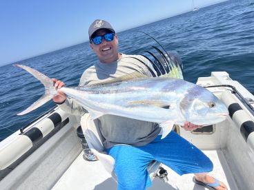 Angler proudly displaying a large Roosterfish while seated on a boat, showcasing the vibrant colors of the fish against the ocean backdrop.