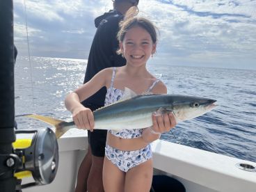 A young angler joyfully displaying a caught fish while fishing on a boat, showcasing a beautiful day at sea.