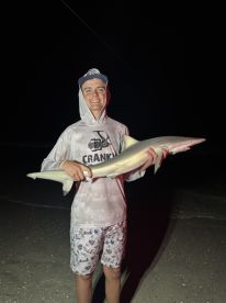 A young angler proudly displaying a shark caught during a nighttime beach fishing session.