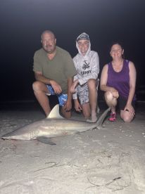 A family poses proudly with a large shark caught during a night fishing trip on the beach.