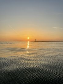 A serene sunset over calm waters, featuring a distant lighthouse, creating a picturesque fishing environment.
