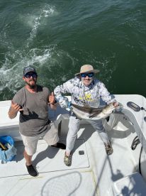 Two anglers celebrating a successful catch of a large Snook aboard a fishing boat, showcasing the excitement of a day on the water.