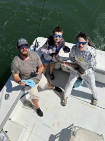 A family of three proudly displaying their catch on a fishing boat, showcasing a large fish while enjoying a sunny day on the water.