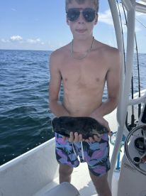 A young angler proudly displaying a black fish while aboard a fishing boat, enjoying a sunny day on the water.