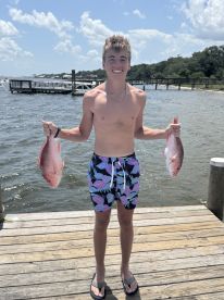 A young angler proudly displaying two Red Snapper at the dock, showcasing a successful fishing trip.
