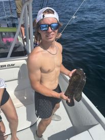 A young angler proudly displaying a large Grouper while fishing on a charter boat in sunny waters.
