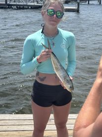 Young angler proudly displaying a caught fish at the dock, showcasing a sunny day on the water.