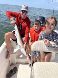 A proud moment on a fishing trip with a family, showcasing a caught shark while enjoying a sunny day on the water.