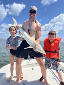 A proud family moment on the boat with a young angler holding a large shark, showcasing their successful catch during a fun day on the water.